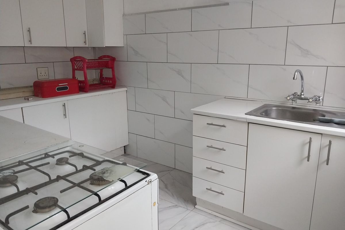A functional kitchen featuring white cabinetry, marble-look wall and floor tiling, and a stainless steel sink with a gas stove.