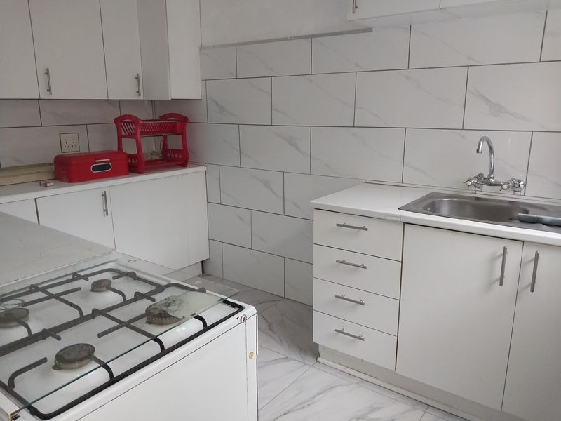 A functional kitchen featuring white cabinetry, marble-look wall and floor tiling, and a stainless steel sink with a gas stove.
