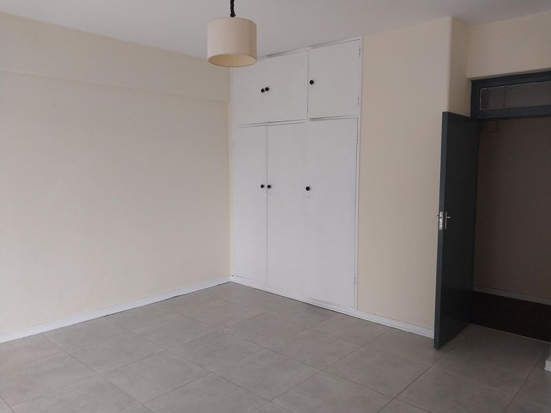 An empty bedroom featuring neutral walls, tiled flooring, and white built-in cupboards providing ample storage space.