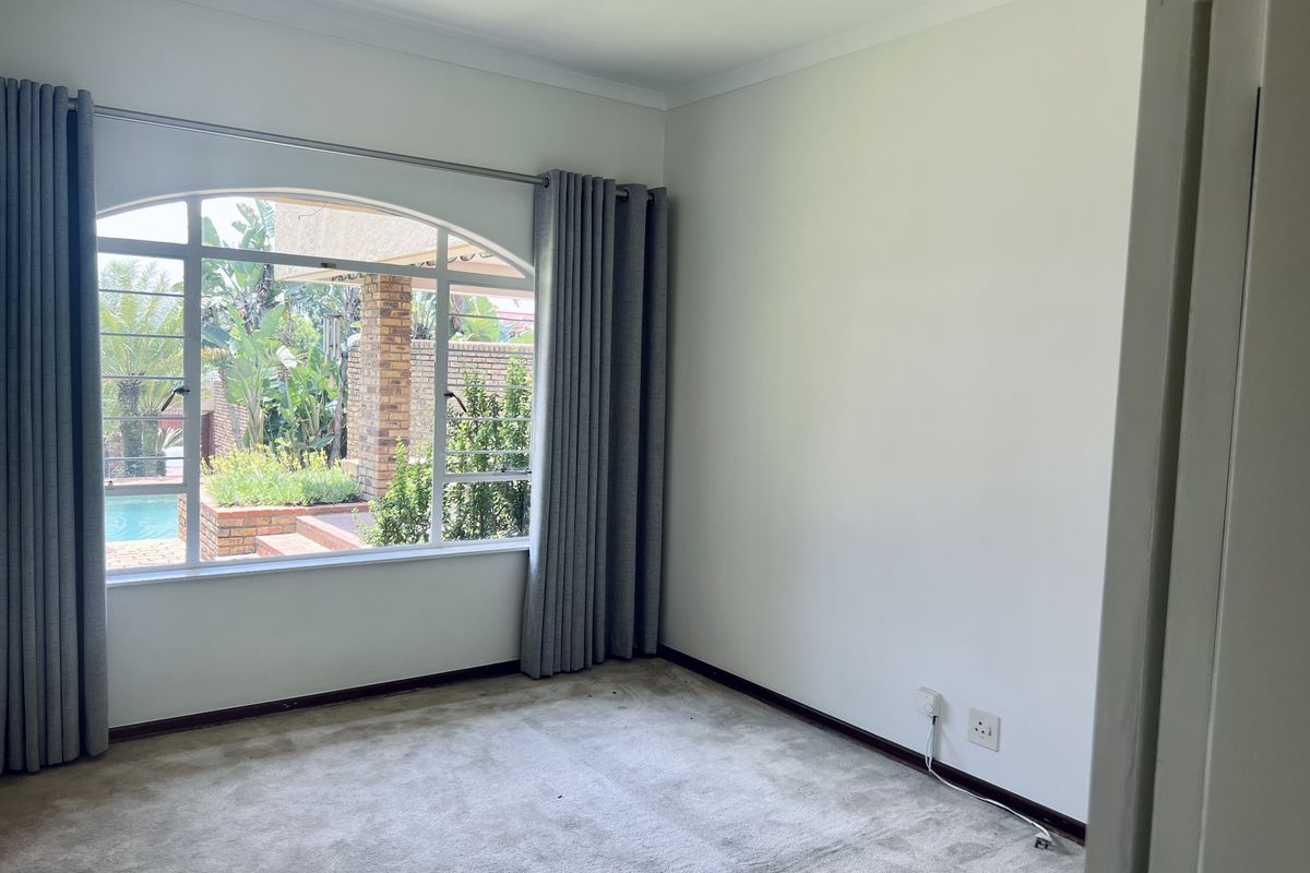 A bright, empty bedroom featuring a large arched window with garden and pool views, neutral walls, and carpeted flooring.