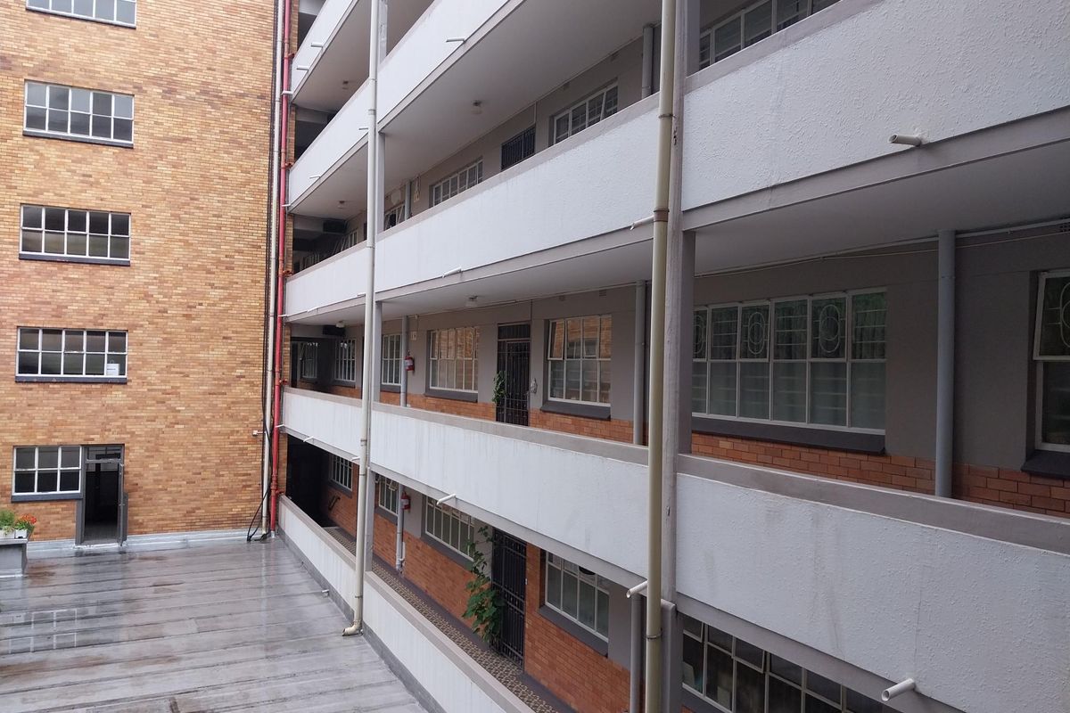 Exterior view of a multi-story apartment building featuring brick facade, open walkways, and metal window frames.