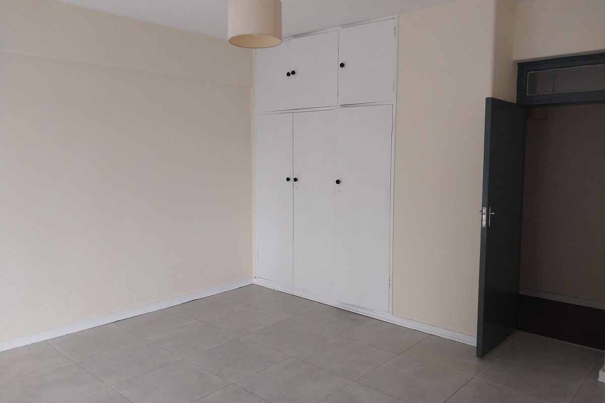 A bright, empty bedroom featuring neutral tiled flooring, built-in white storage cabinetry, and a simple pendant light fixture.