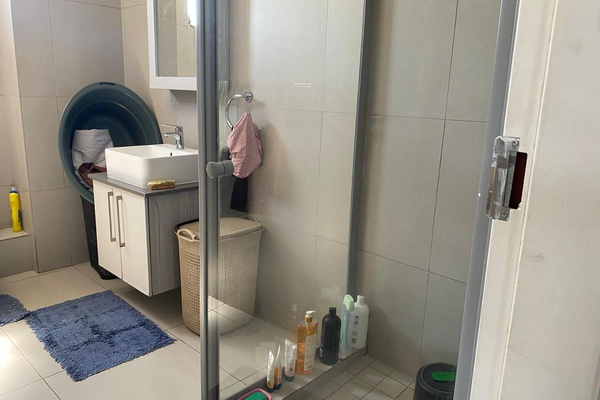 A functional bathroom featuring a modern vanity with basin, a glass-enclosed shower, and neutral wall tiling.