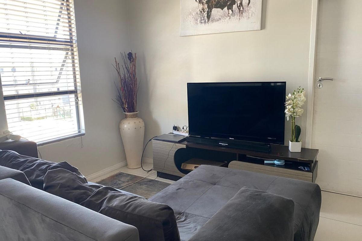 A comfortable living room featuring tiled flooring, a large window with fitted blinds, and a neutral wall finish.