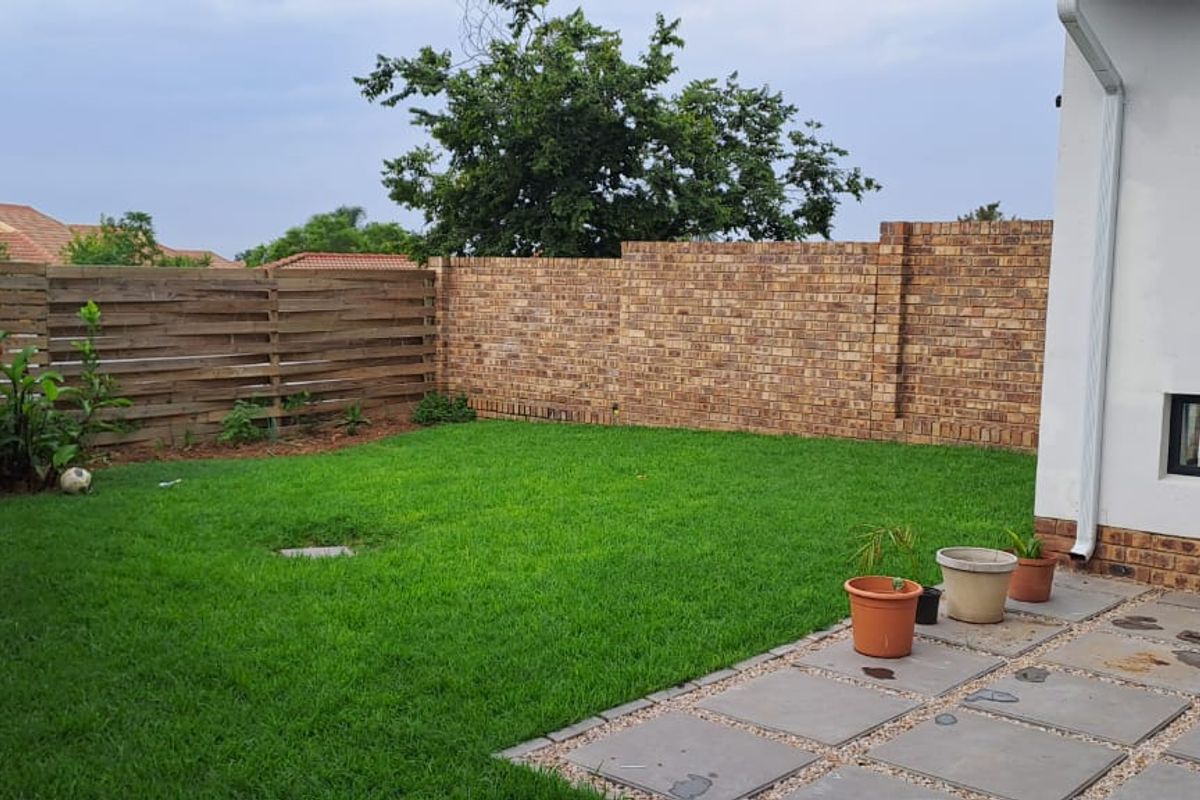 A private rear garden featuring a paved patio area, a well-maintained lawn, and perimeter brick and timber fencing with security electric fencing.