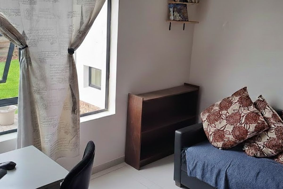 A functional living space featuring large windows with garden views, tiled flooring, and neutral wall finishes.