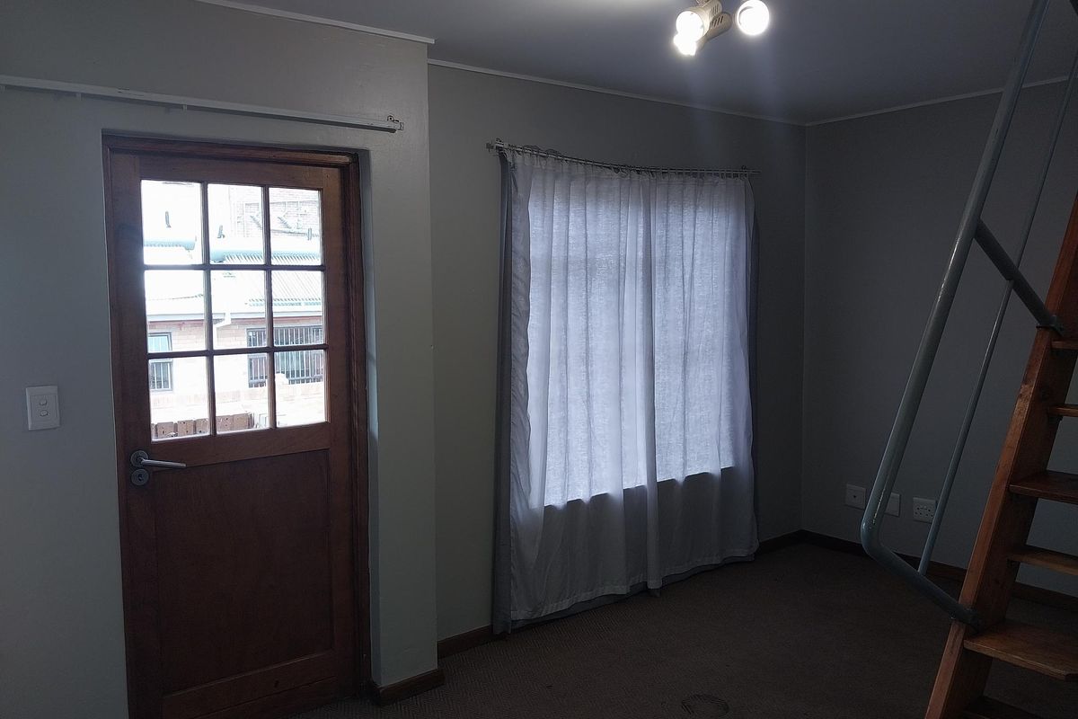A living area featuring a wooden door, large window with curtains, and a wooden staircase leading to an upper level.