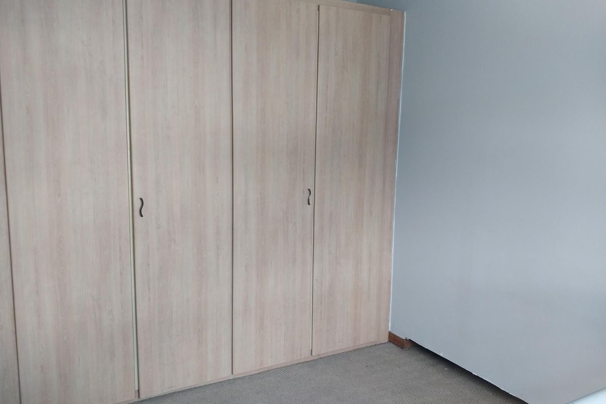 A bedroom featuring built-in light wood-grain wardrobes and neutral wall finishes.