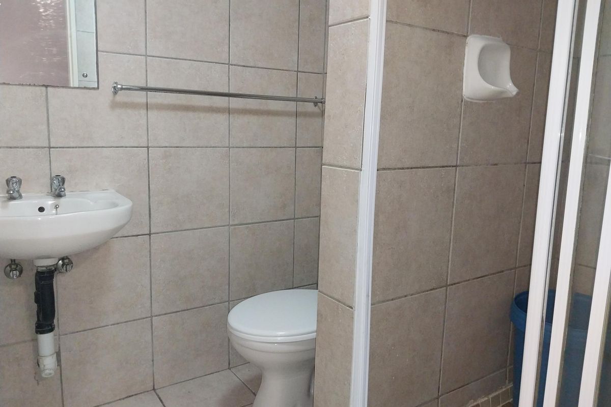 A functional bathroom featuring tiled walls, a wall-mounted basin, a toilet, and a shower enclosure.