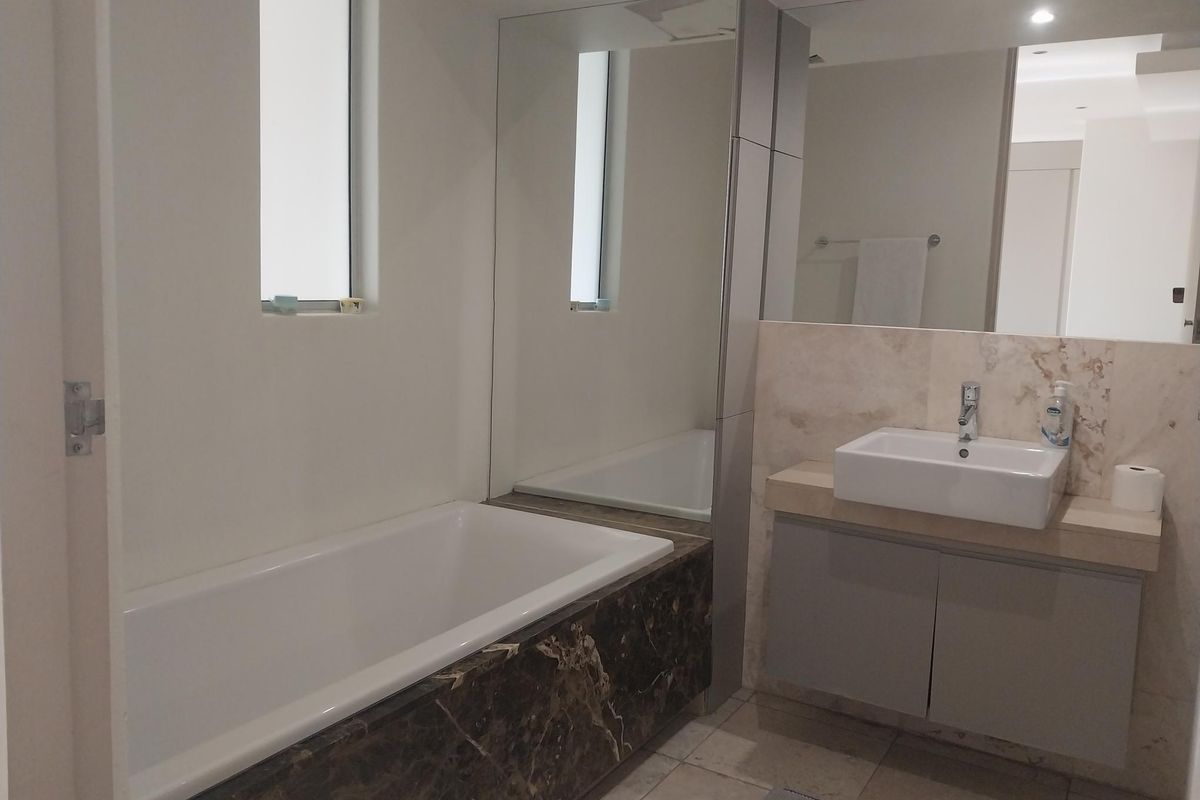 Modern bathroom featuring a built-in bathtub with dark marble cladding, a floating vanity with a vessel sink, and large wall-mounted mirrors.