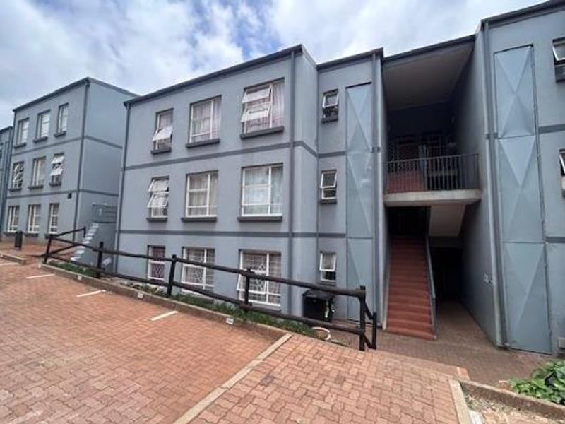 Exterior view of a multi-story apartment complex featuring paved driveway access, external staircases, and grey painted facade with casement windows.