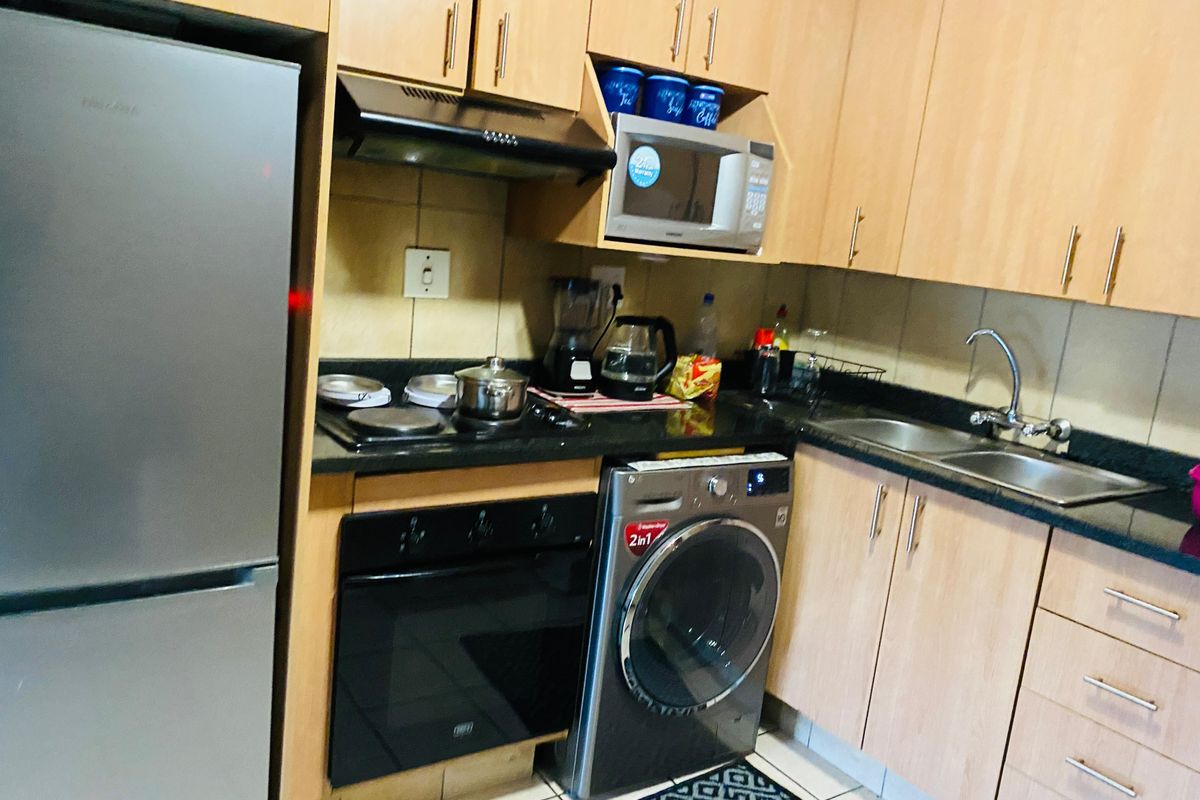 Compact kitchen featuring laminate cabinetry, granite countertops, built-in oven, hob, extractor fan, and integrated laundry appliance space.
