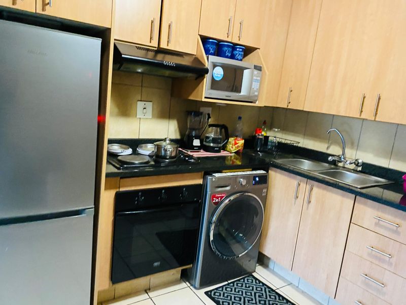 Compact kitchen featuring laminate cabinetry, granite countertops, built-in oven, hob, extractor fan, and integrated laundry appliance space.