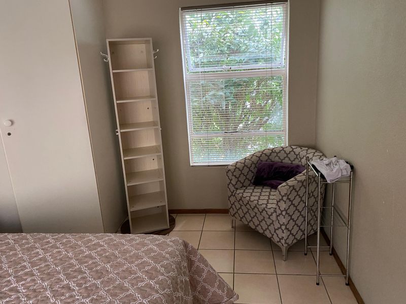 A bedroom featuring tiled flooring, a built-in wardrobe, and a window with fitted blinds, offering a functional and neutral living space.