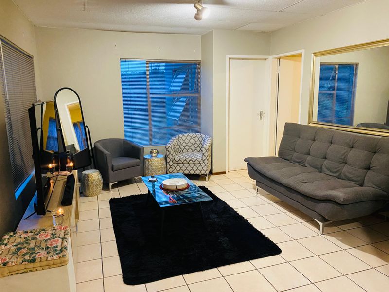 A living room featuring tiled flooring, venetian blinds, and a ceiling-mounted spotlight, offering a functional space with potential for cosmetic updates.