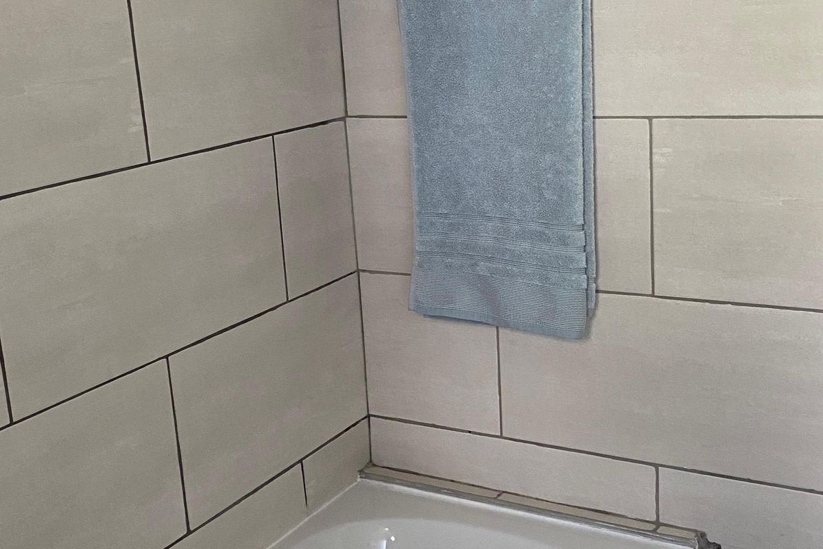 A clean bathroom featuring a built-in bathtub with modern light-toned ceramic wall tiling and a chrome towel rail.
