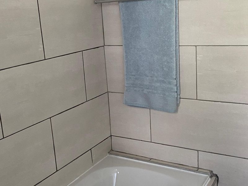 A clean bathroom featuring a built-in bathtub with modern light-toned ceramic wall tiling and a chrome towel rail.