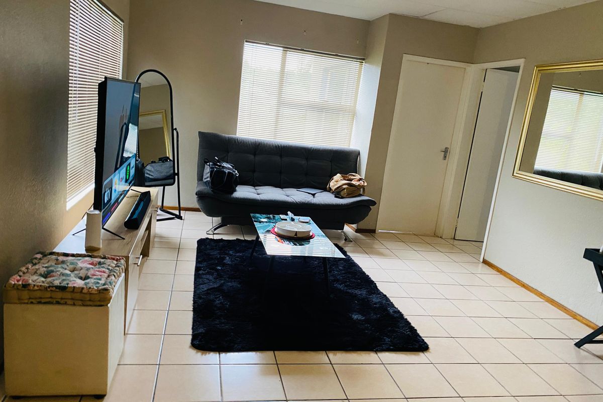 A living room featuring tiled flooring and natural light through venetian blinds, offering a functional space ready for cosmetic updates.