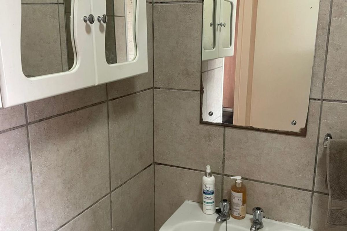 A compact bathroom featuring a wall-mounted basin, a mirrored medicine cabinet, and neutral wall tiling.