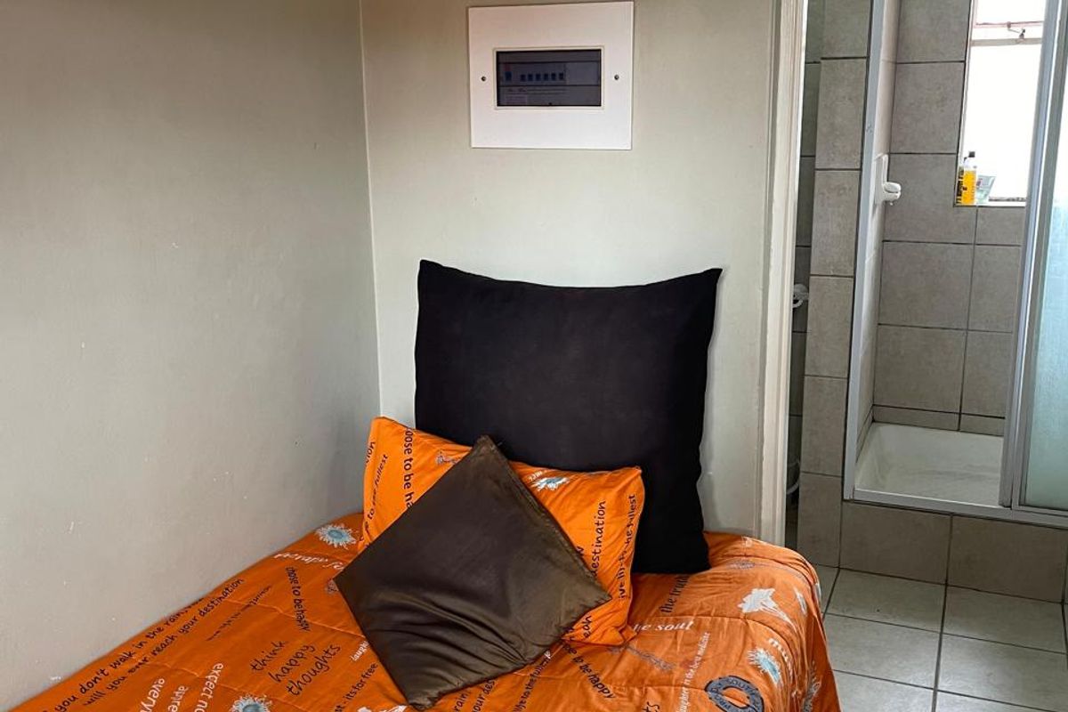 A bedroom featuring tiled flooring and an en-suite bathroom with a shower cubicle, including a wall-mounted electrical distribution board.