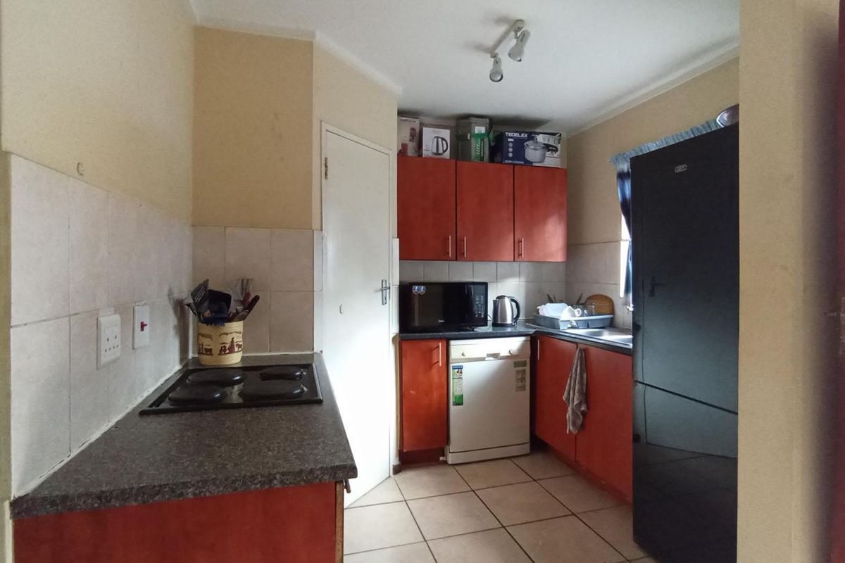 A compact kitchen featuring wooden cabinetry, laminate countertops, an electric hob, and tiled flooring, offering a functional layout with potential for modernization.