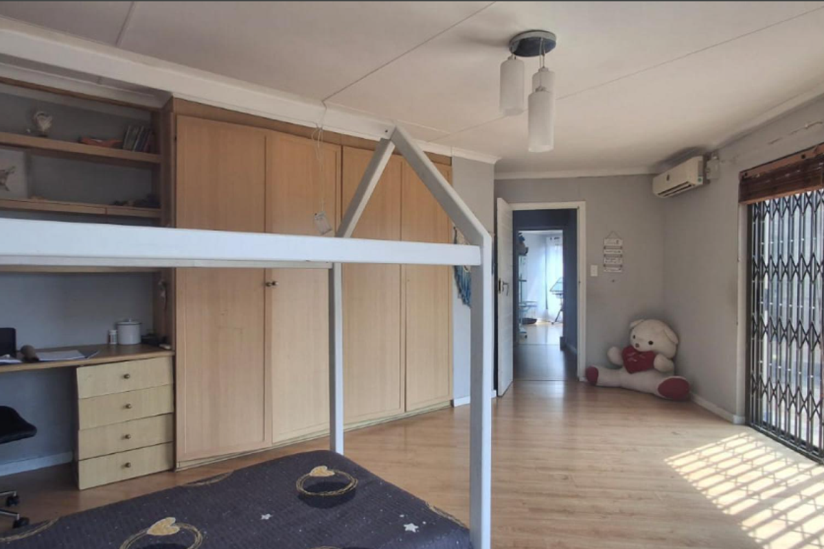 Bedroom featuring built-in cupboards, a study desk, laminate flooring, and an air conditioning unit, with access to an outdoor area via a security gate.