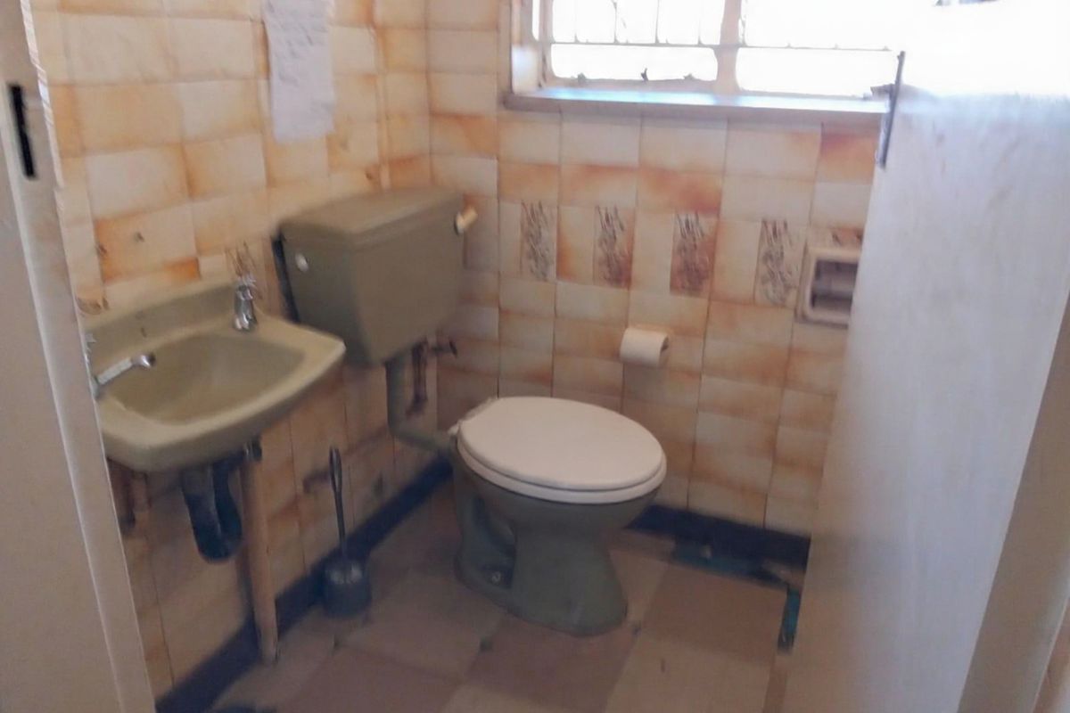 A dated bathroom featuring original wall tiling, a vintage basin, and a standard toilet suite, requiring significant modernization and renovation.