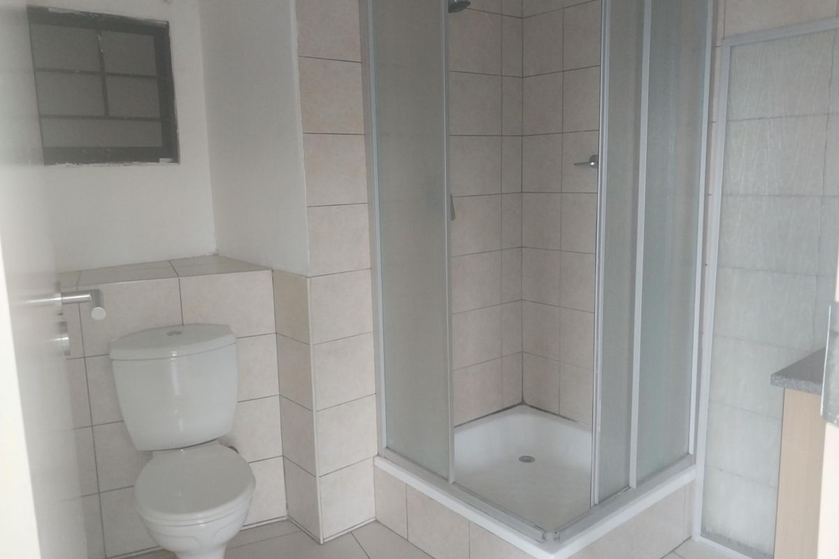 A functional bathroom featuring a tiled shower enclosure with a glass door, a standard toilet, and neutral wall and floor tiling.