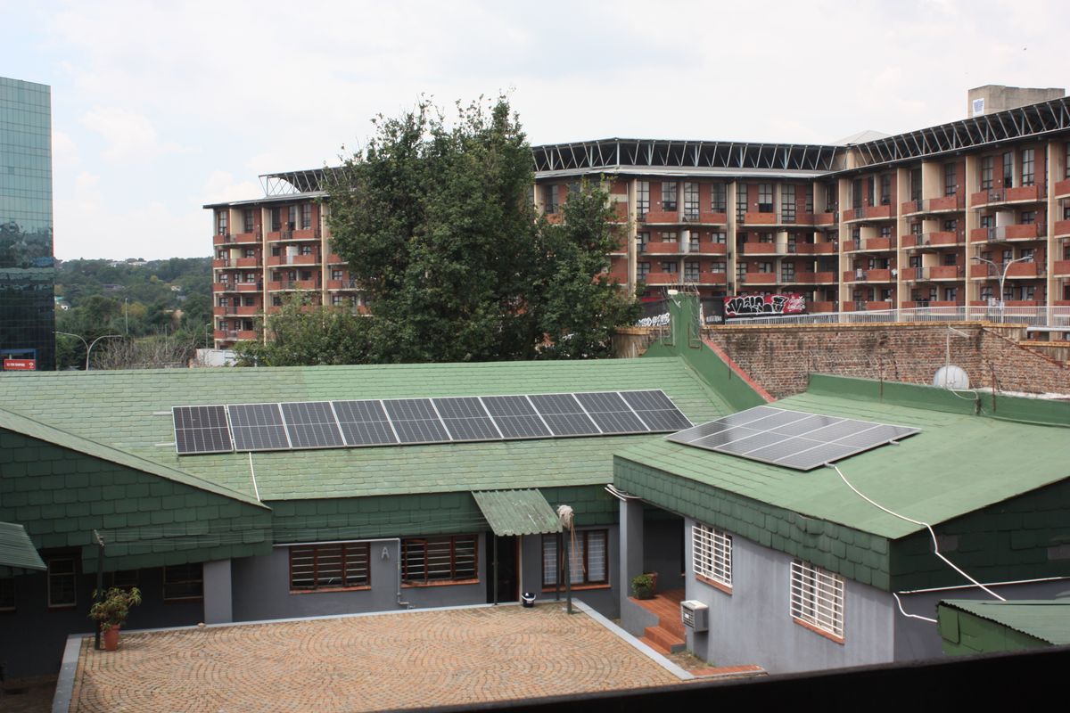 An elevated view of the property featuring a green shingled roof equipped with solar panels and a paved courtyard area.