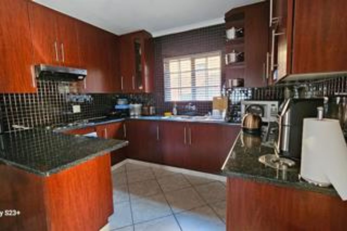A functional kitchen featuring dark wood cabinetry, granite countertops, a tiled backsplash, and a breakfast nook area.