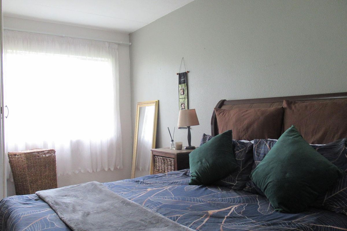 A well-lit bedroom featuring neutral wall finishes and a large window, providing a comfortable and functional sleeping space.