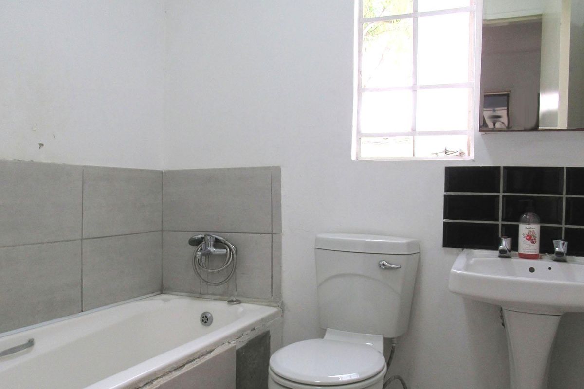 A functional bathroom featuring a standard bathtub, pedestal basin, and toilet, with a window providing natural light.