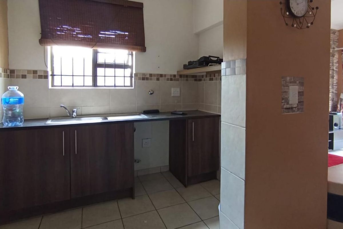 A functional kitchen area featuring dark wood-finish cabinetry, a stainless steel sink, and tiled splashbacks, adjacent to the main living space.