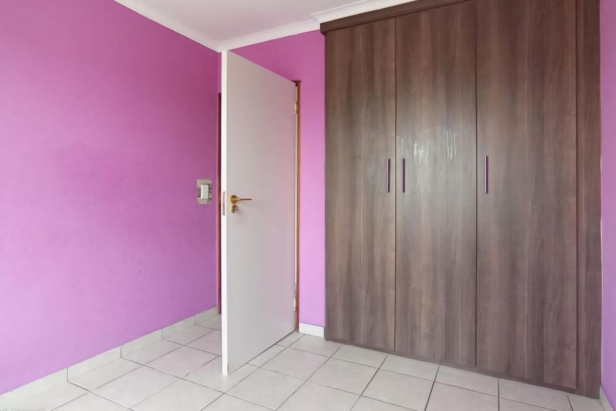 A bedroom featuring built-in wooden cupboards, tiled flooring, and bright purple painted walls.