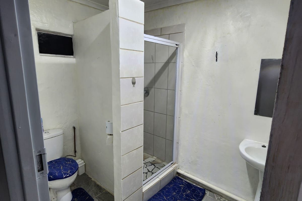 A functional bathroom featuring a shower enclosure, pedestal basin, and toilet with tiled flooring and basic lighting fixtures.