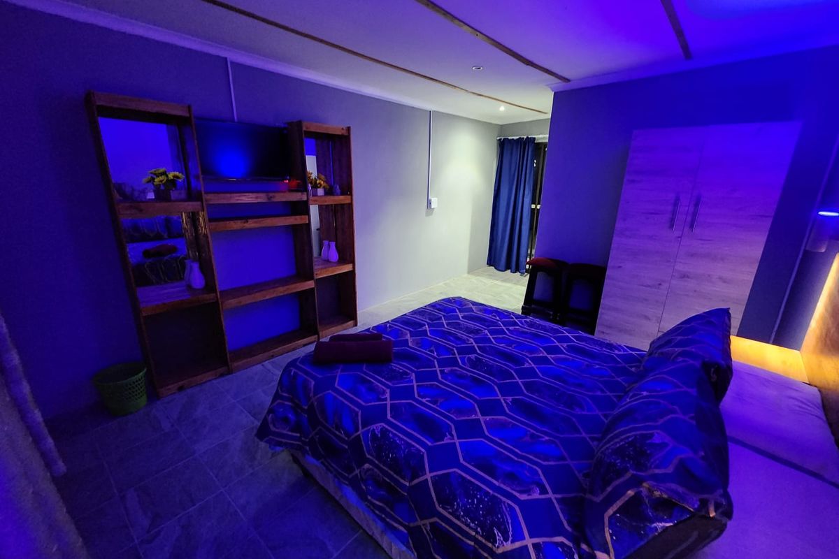A bedroom featuring tiled flooring and a built-in wardrobe, illuminated with ambient blue lighting.