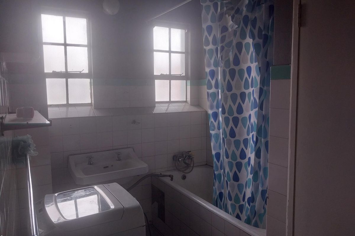 A dated bathroom featuring a bathtub with shower attachment, wall-mounted basin, and tiled walls, with space for a top-loading washing machine.