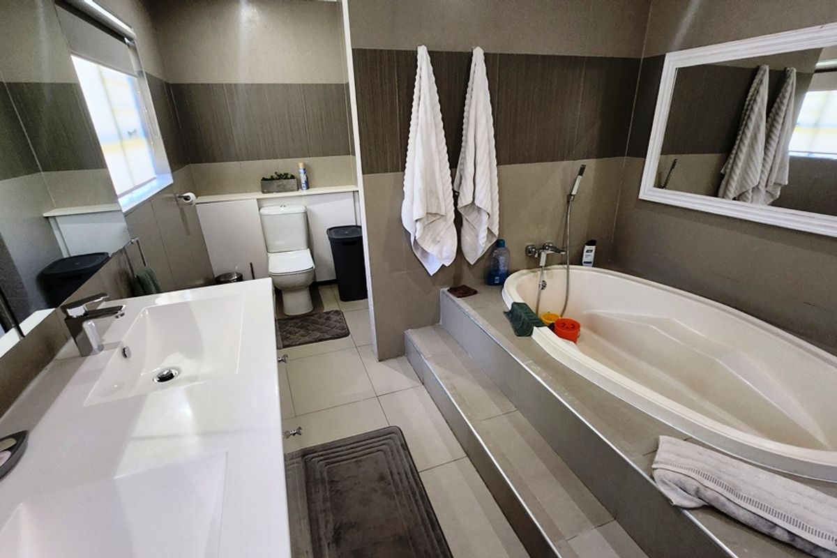 A functional bathroom featuring a built-in bathtub, vanity basin, and toilet with neutral wall and floor tiling.