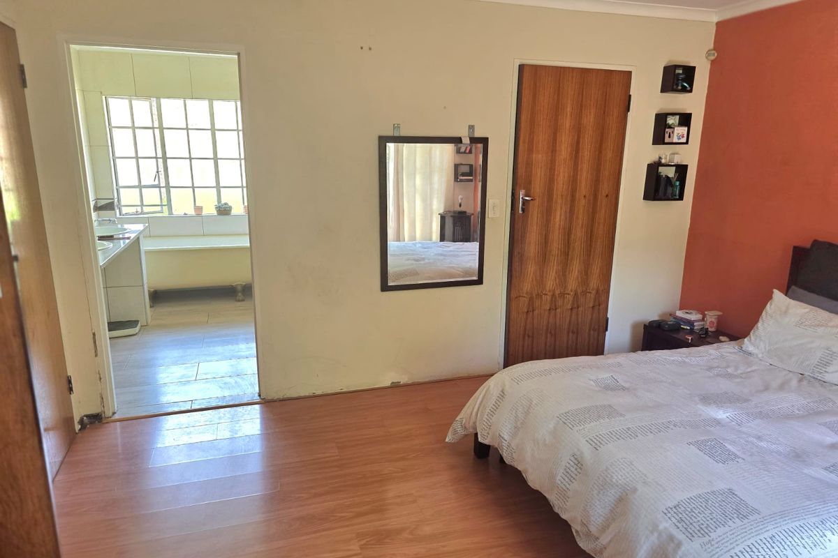 Bedroom featuring laminate flooring and direct access to an en-suite bathroom, showing signs of wear on the ceiling and walls.