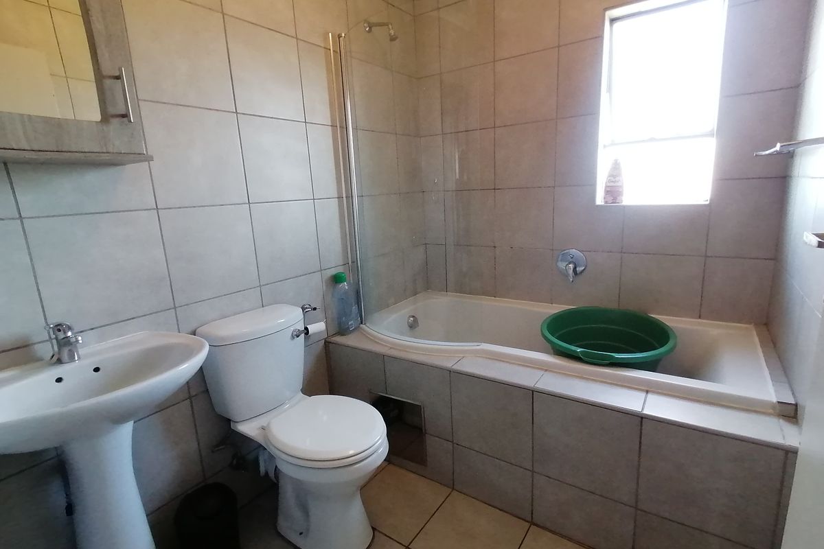 A functional bathroom featuring a pedestal basin, toilet, and a bathtub with an integrated shower and glass screen.