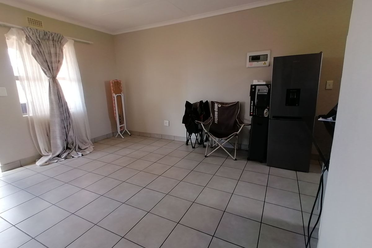 A tiled living area featuring neutral walls, a window with curtains, and a built-in electrical distribution board.