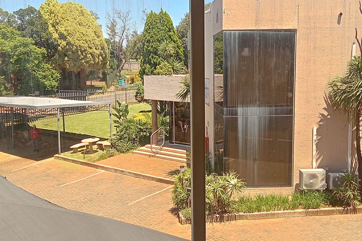 An elevated view of the property exterior, featuring a paved driveway, covered parking area, and landscaped garden space.