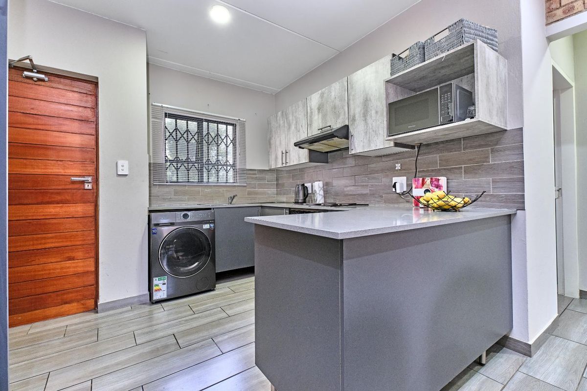 Modern kitchen featuring grey cabinetry, stone-look countertops, tiled backsplash, integrated laundry plumbing, and a breakfast bar island.