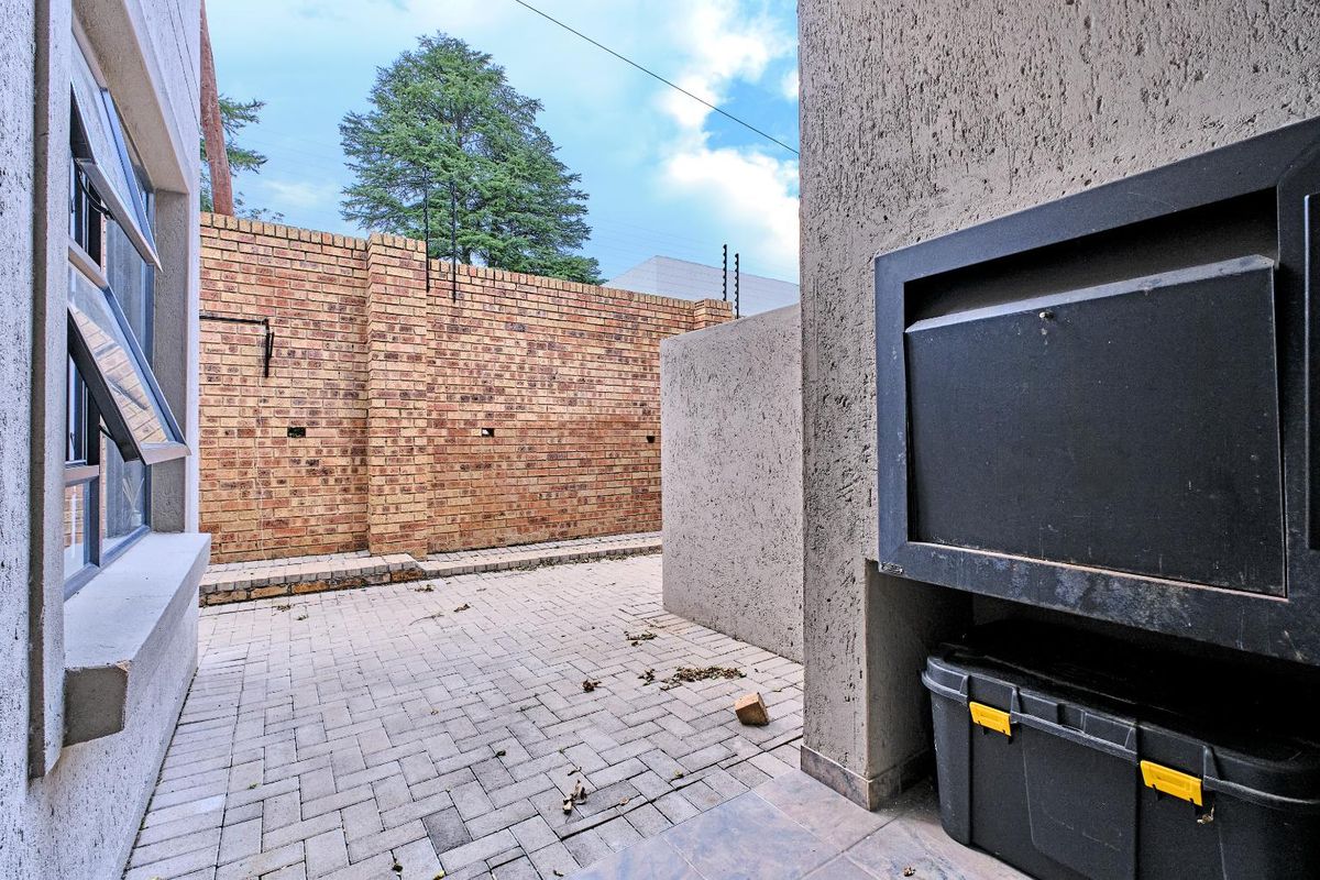 A private rear courtyard featuring paved flooring, a built-in braai, and high perimeter brick walls with security fencing.
