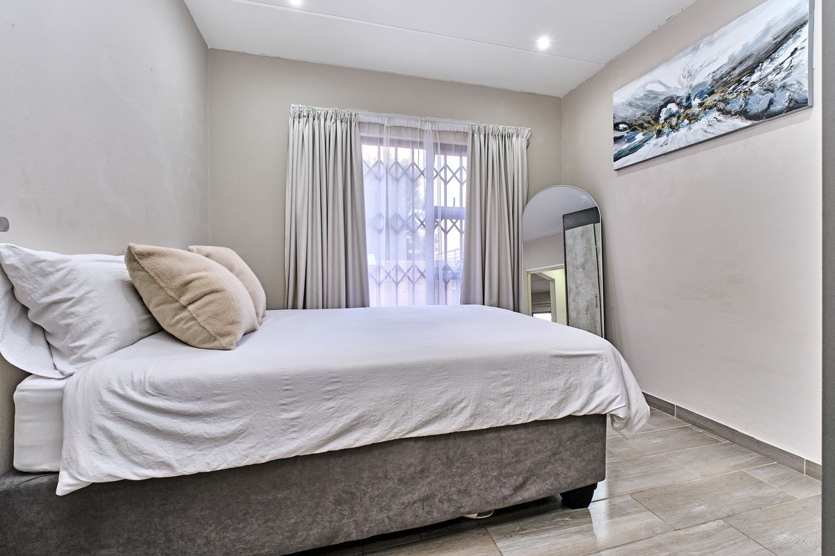 A well-maintained bedroom featuring neutral wall tones, tiled flooring, and a window fitted with security bars and curtains.