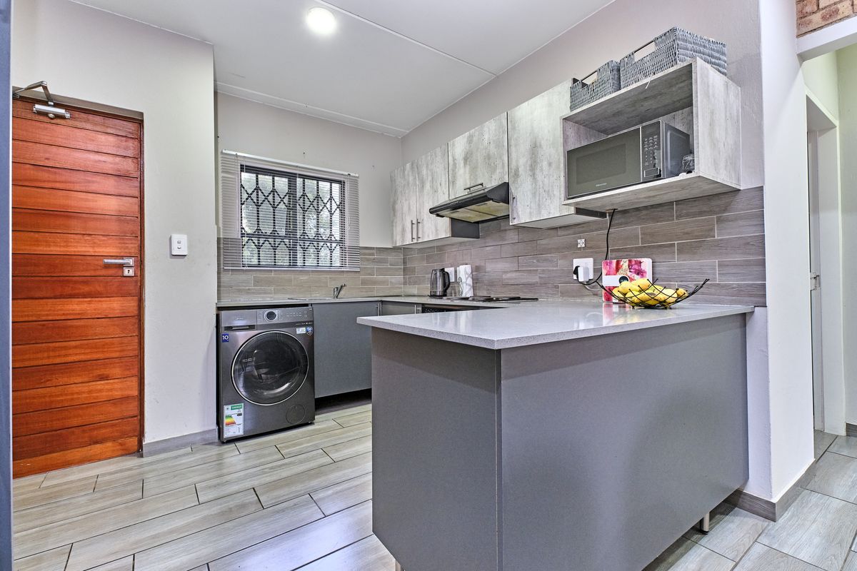 Modern kitchen featuring grey cabinetry, stone-look countertops, tiled backsplash, built-in extractor fan, and integrated laundry plumbing.
