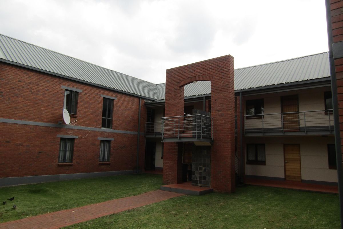 Exterior view of a brick apartment complex featuring a central courtyard, metal roofing, and balcony access with metal railings.