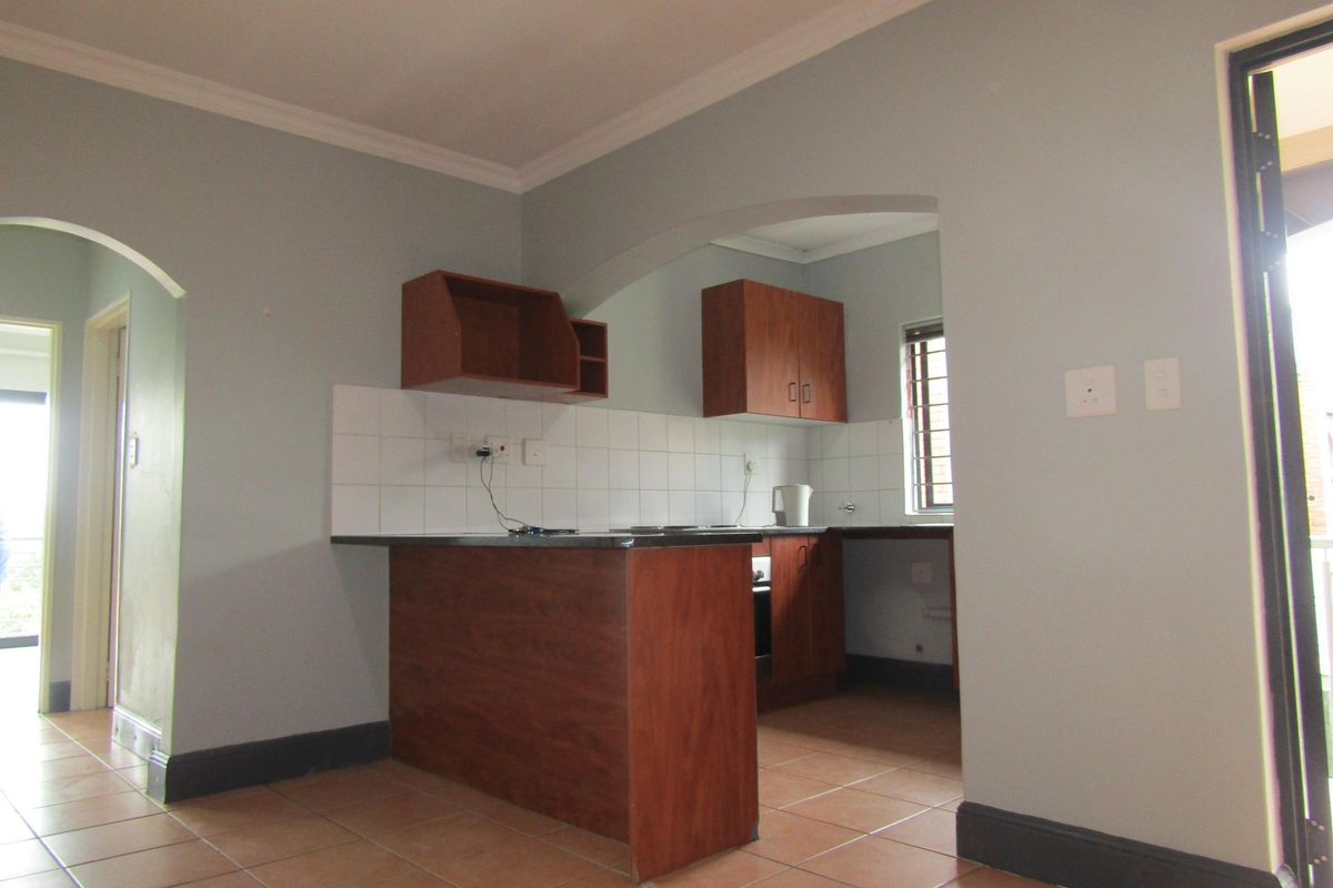 A functional kitchen featuring wooden cabinetry, tiled splashbacks, and a breakfast bar, connected to the living area through an arched doorway.