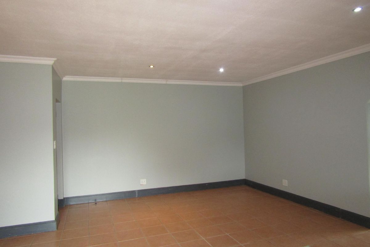 A spacious, empty living area featuring neutral wall tones, dark skirting boards, and tiled flooring with recessed ceiling downlights.