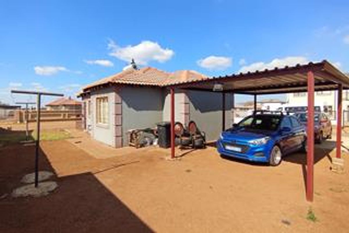 Rear exterior view of the house featuring a metal carport structure and a paved pathway surrounding the building.